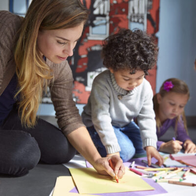 Teacher Drawing On Papers With Students At Preschool
