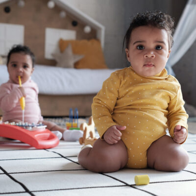 Selective focus shot of two lovely twin babies sitting on floor in loft kids room looking at camera